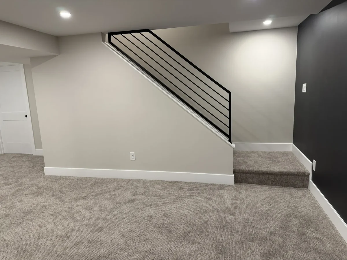 After: the finished lower level with painted walls, recessed lighting, carpet and an open staircase with a black steel rail.