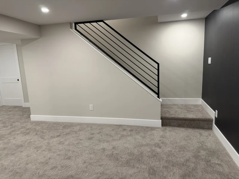 After: the finished lower level with painted walls, recessed lighting, carpet and an open staircase with a black steel rail.
