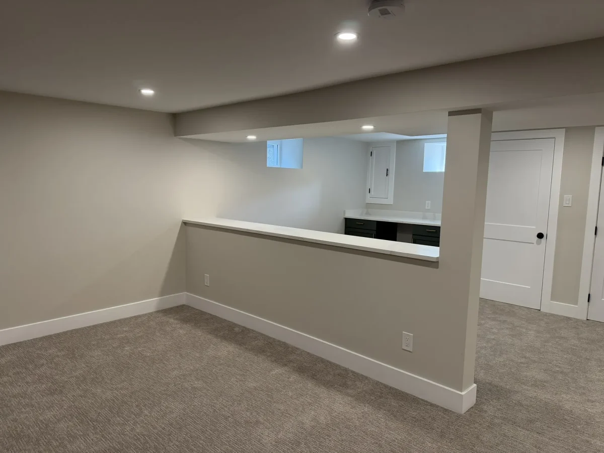 Finished basement family area with a half-wall divider, recessed lights and wall-to-wall carpet.