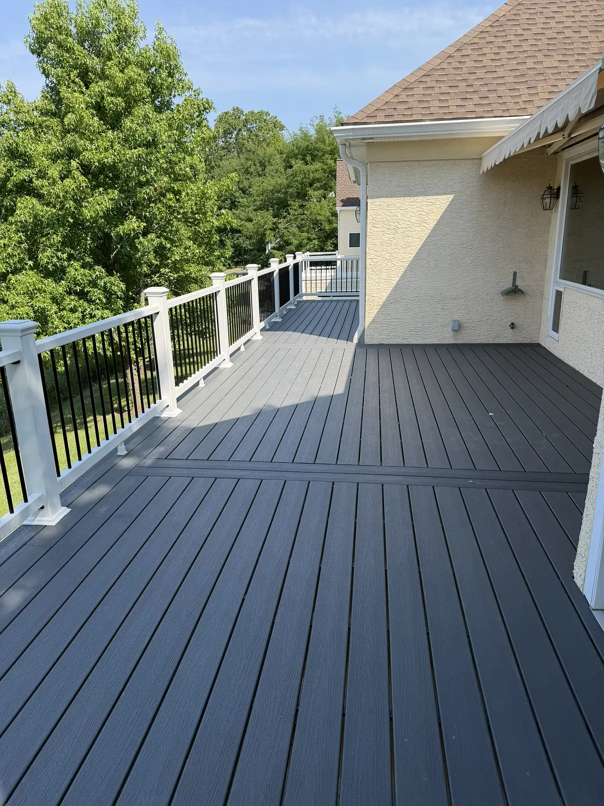 Grey composite deck running the width of a house, edged with white railing and turned posts.