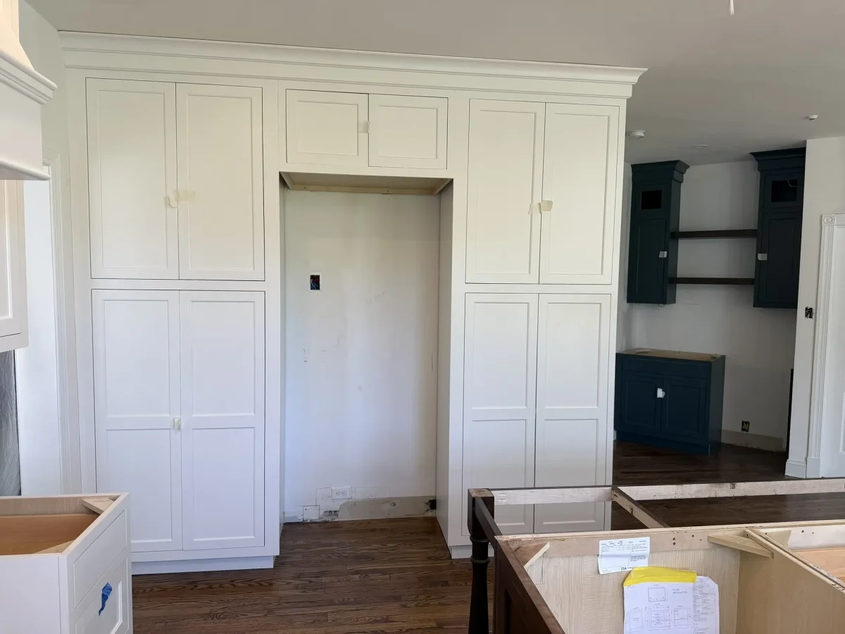 Full-height white built-in cabinetry framing a doorway, with a navy painted alcove and open shelving to one side.