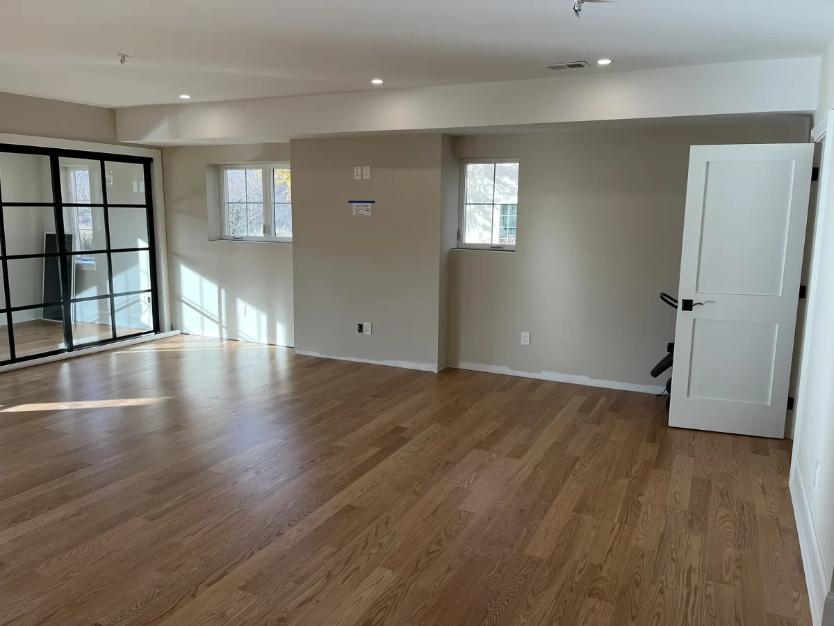 Adjoining living space with black-framed glass doors, fresh white trim and unfurnished oak flooring.