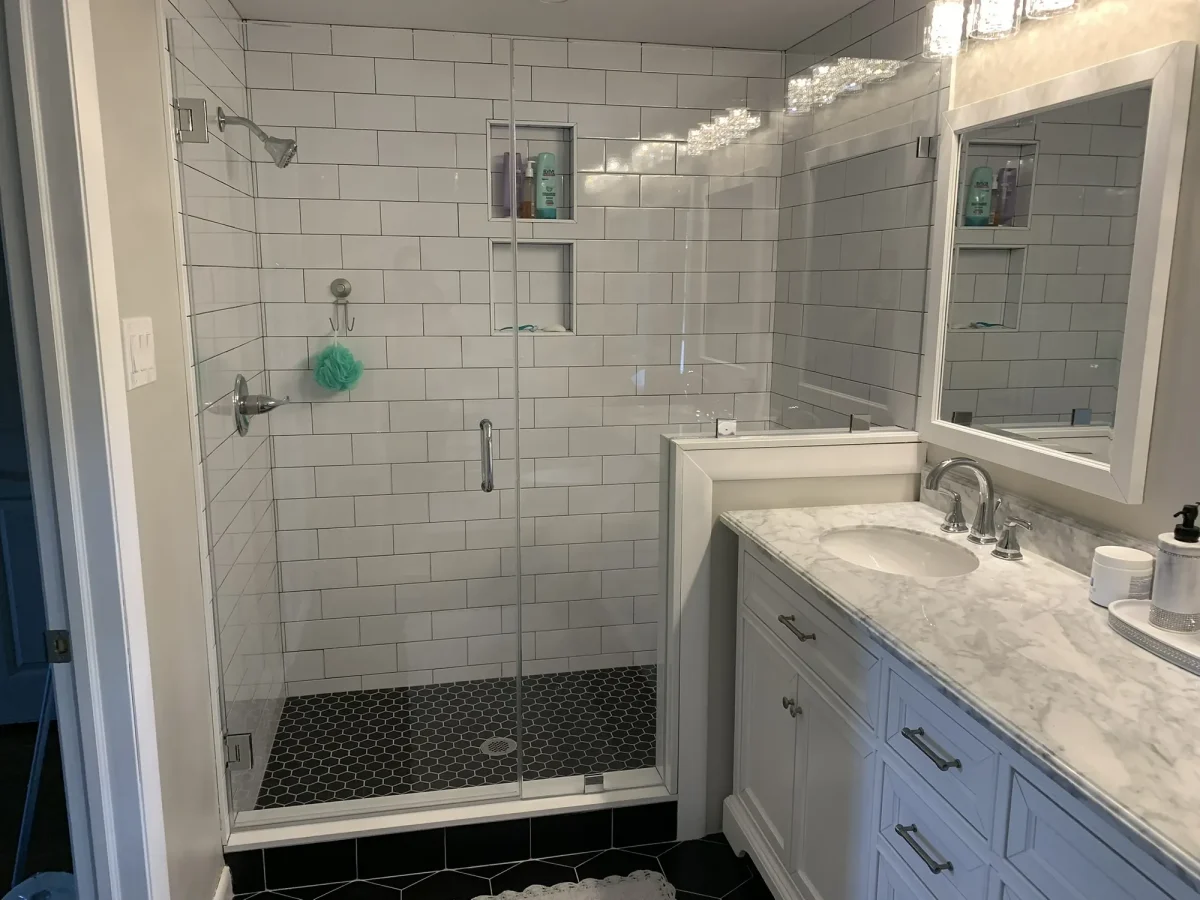 Glass-enclosed shower lined in white subway tile with a built-in niche, beside the marble-topped vanity.