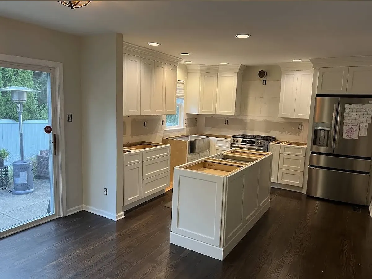 White shaker kitchen with a large central island on dark hardwood floors, sliding glass doors to the garden at the far end.