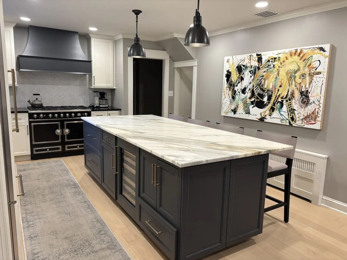 Wide view of the finished kitchen showing the island seating, dark cabinetry base and a large painted canvas on the far wall.