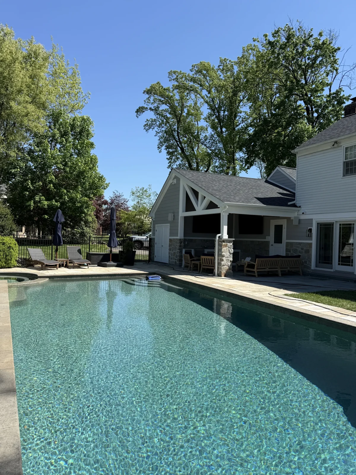 Long rectangular pool in full sun with the pavilion and mature trees behind it.